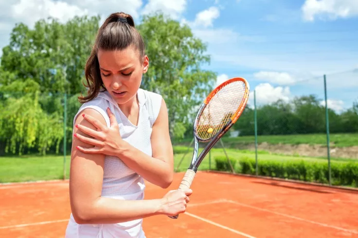 A woman on a tennis court holding her shoulder in pain